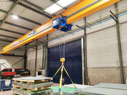 I en industrilokal lyfter en talj på en enkelbalk-kranvagn av typ ELV en pall som är fastsatt med fyra band.