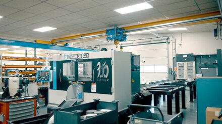 En fabrikshall med verktygsmaskiner. På en kranbana kör en brokran av typ ELV med en elektrisk linlyft av typ E.