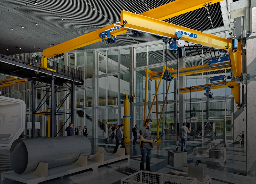 I expoområdet i KranHaus i Gummersbach kan kunderna testa olika typer av kranar under verkliga förhållanden. I förgrunden syns en man som lyfter en tung stålkub med hjälp av en kättingtelfer på en väggsvängkran.