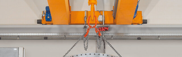 En kranbalk med påbyggnadsdelar, till vilken en kedjeupphängning med last är fäst.