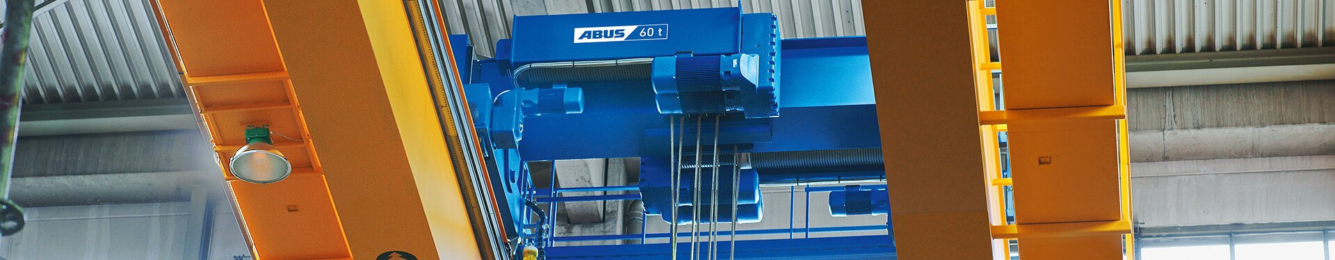 Vy underifrån på en tvåskenig kranvagn av typ Z med dubbelt lyftverk och en bärförmåga på 60 ton på en brokran av typ ZLK. På båda huvudbalkarna finns gångbroar monterade. Under en av dessa gångbroar är en LED-strålare installerad.