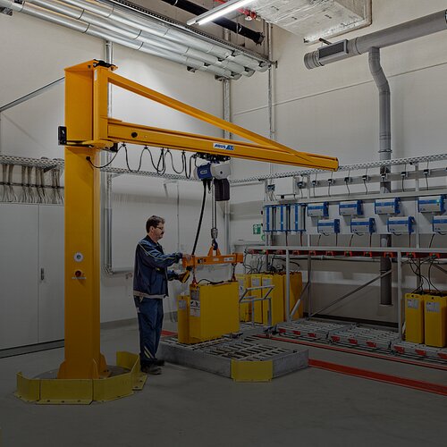 En medarbetare manövrerar en pelarsvängkran och flyttar en last vid en arbetsplats i en industrihall