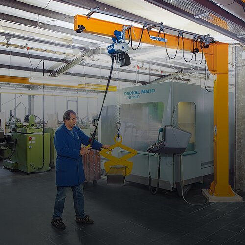 En medarbetare manövrerar en pelarsvängkran och lyfter en last med en kedjehiss i en fabrikshall.