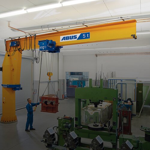 En medarbetare manövrerar en pelarsvängkran och lyfter en tung last med en kedjelift i en fabrikshall