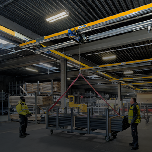 En ZHB-tvärbalkkran lyfter en last i en industrihall medan personalen övervakar arbetet.