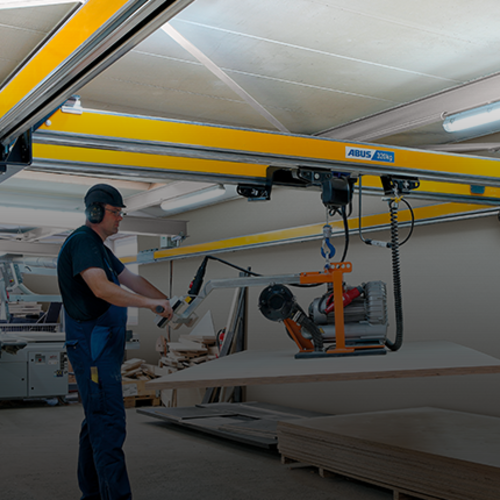 En medarbetare manövrerar en tvåbalkkran av typen ZHB-X och lyfter en last med en kedjehiss i en fabrikshall.